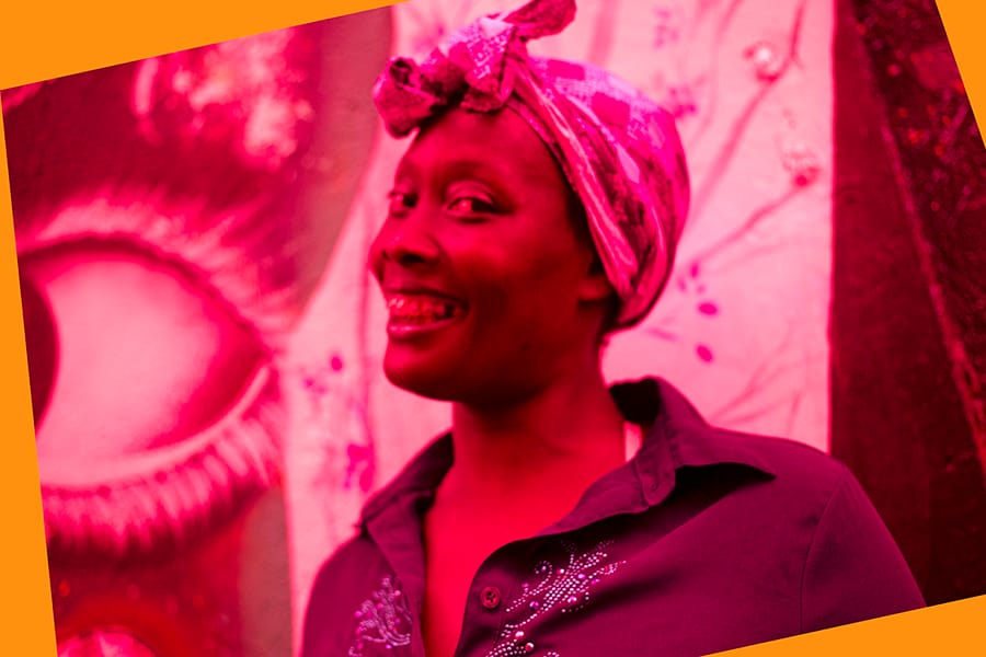 Barriguinha  Portrait of a smiling woman in front of colorful street art at Beco do Batman in São Paulo, edited in strong red tones.